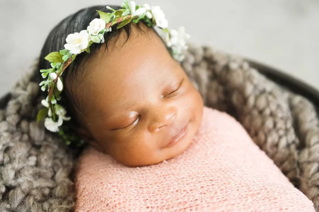 Newborn baby girl in a white flower crown sleeping swaddled in a pink wrap