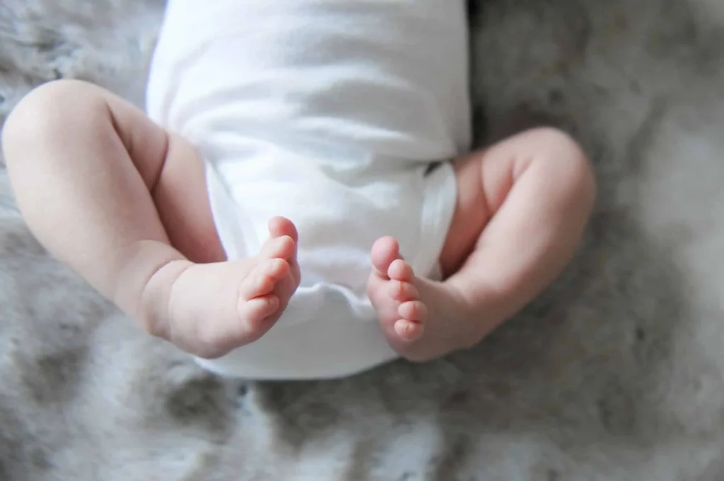Close-up of tiny newborn feet and legs in a white onesie on a soft gray fur