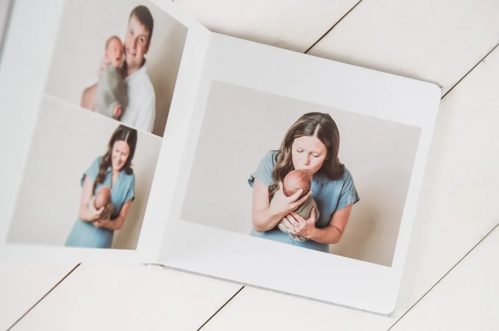 Open photo album on a white wooden surface, showing pictures of a man and woman each lovingly holding and cuddling a newborn baby, with soft, neutral backgrounds in each photo. Kristin Milito Photography - Newborn & Maternity Photographer - Chicago IL