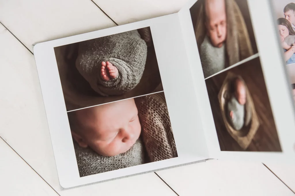 An open photo album by a Chicago Newborn Photographer displays close-up images of a newborn baby wrapped in a knit blanket, featuring the baby’s face and tiny feet, on a white wooden surface. Kristin Milito Photography - Newborn & Maternity Photographer - Chicago IL