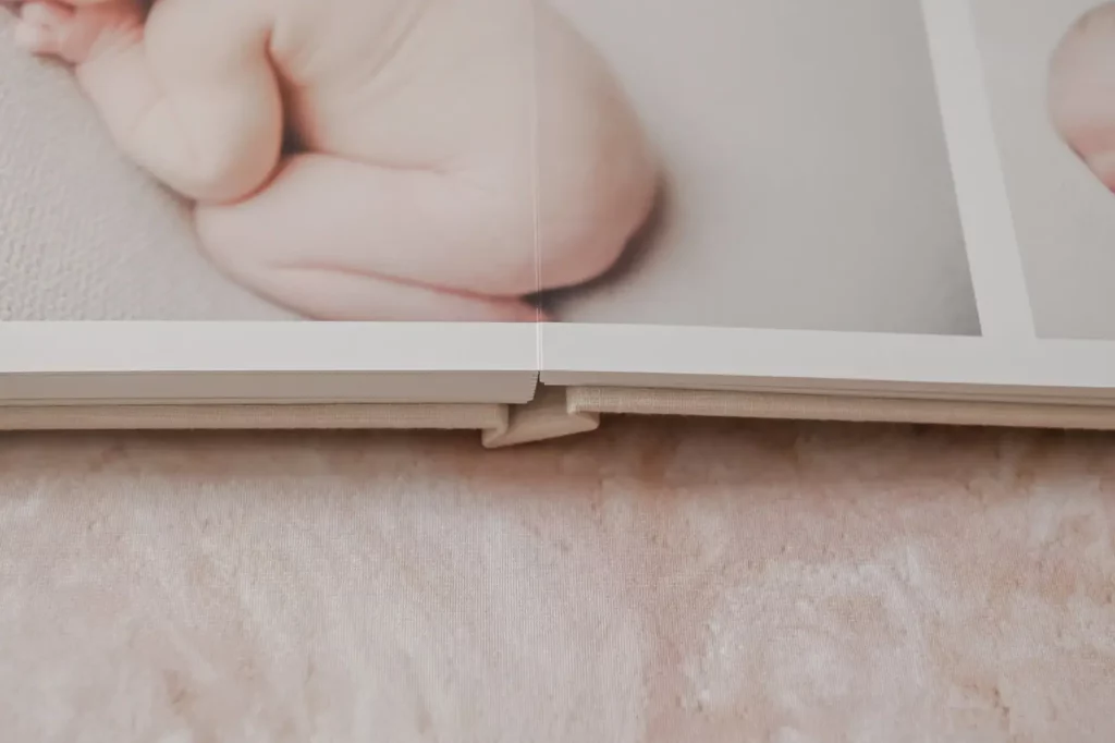 Close-up of an open photo album displaying a soft-focus image of a baby's hand and feet, resting on a light-colored textured surface. Kristin Milito Photography - Newborn & Maternity Photographer - Chicago IL