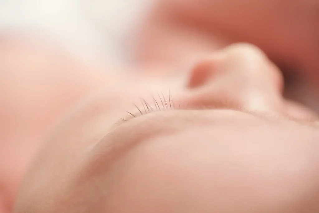 A woman with shoulder-length blonde hair smiles warmly at the camera. She is holding a DSLR camera in her right hand and wearing a denim jacket. The background is a solid, dark color, enhancing the focus on her cheerful expression and professional demeanor. - Image by Kristin Milito Photography, Chicago IL.