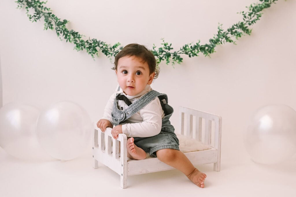 Baby sitting on small bed with balloons.