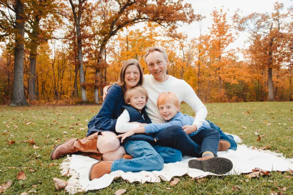 Family sitting on blanket in autumn forest.