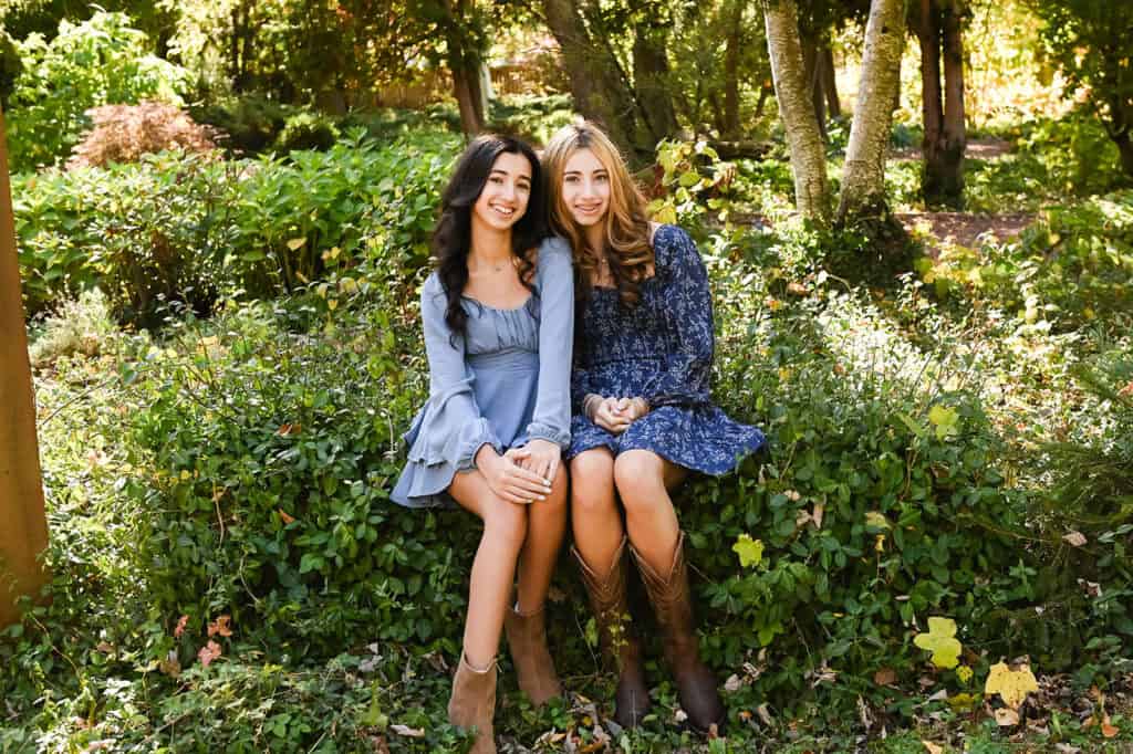 Two women sitting in a lush green garden.