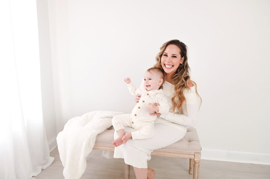 Smiling woman holding baby on bench, bright room.