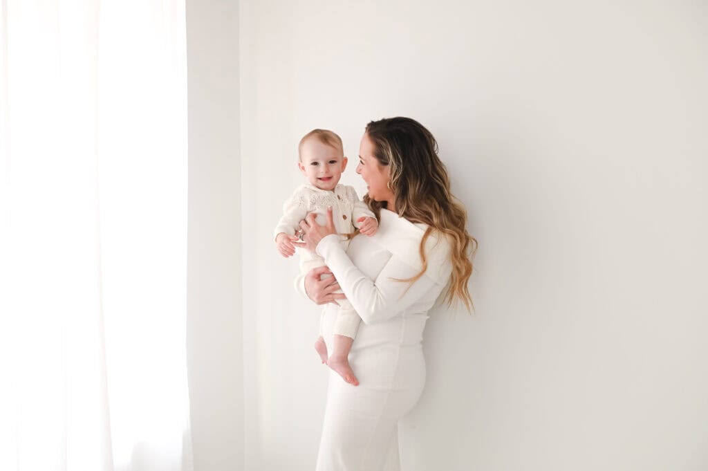 Mother holding smiling baby in white room